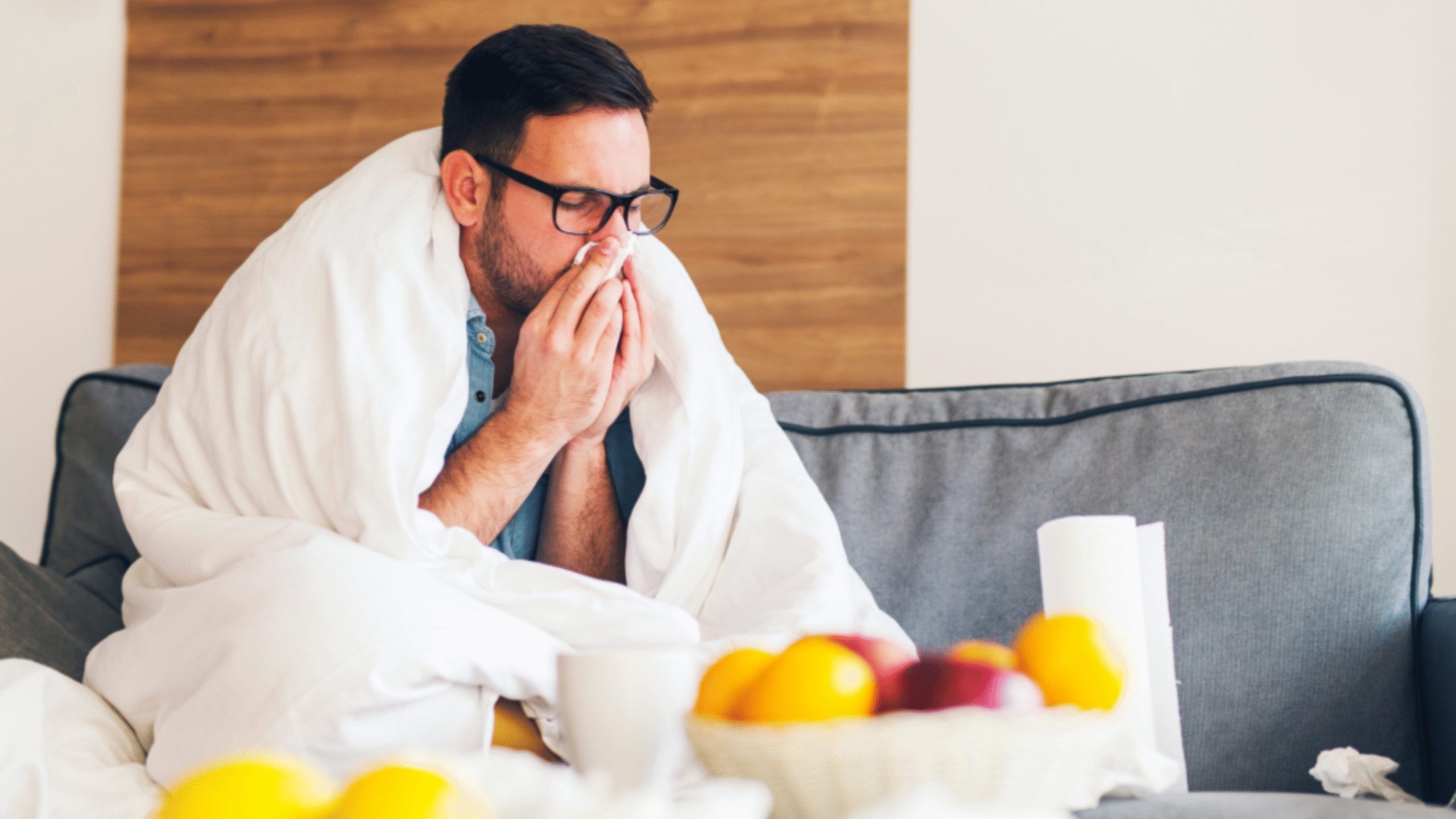 sick man on the couch covered in a blanket blowing his nose