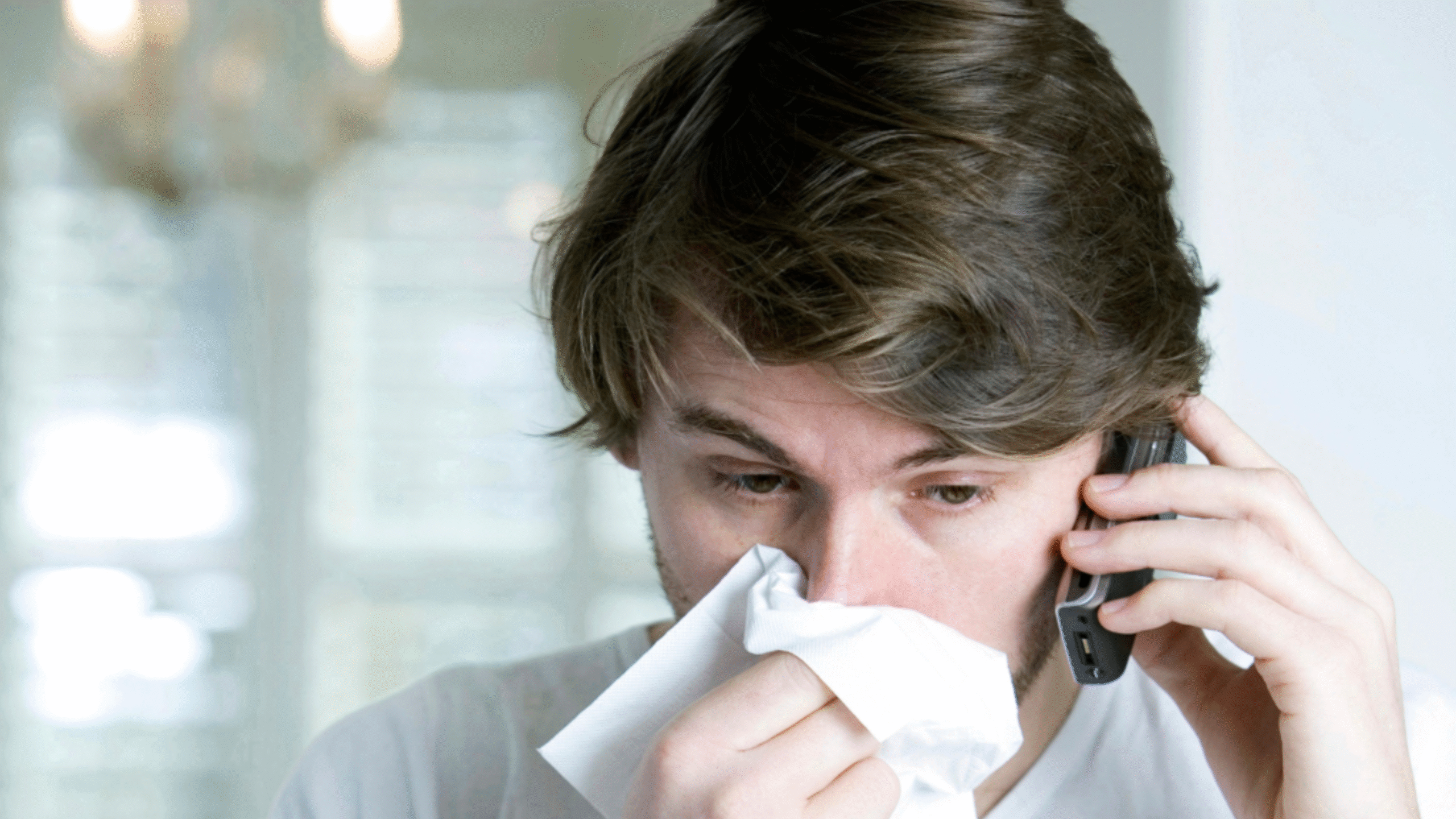 Man blows his nose with a tissue while on the phone