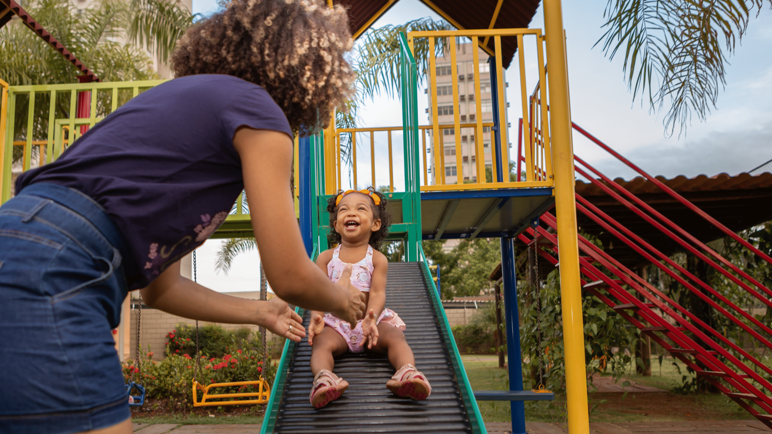 mother helps child down the slide on the playground