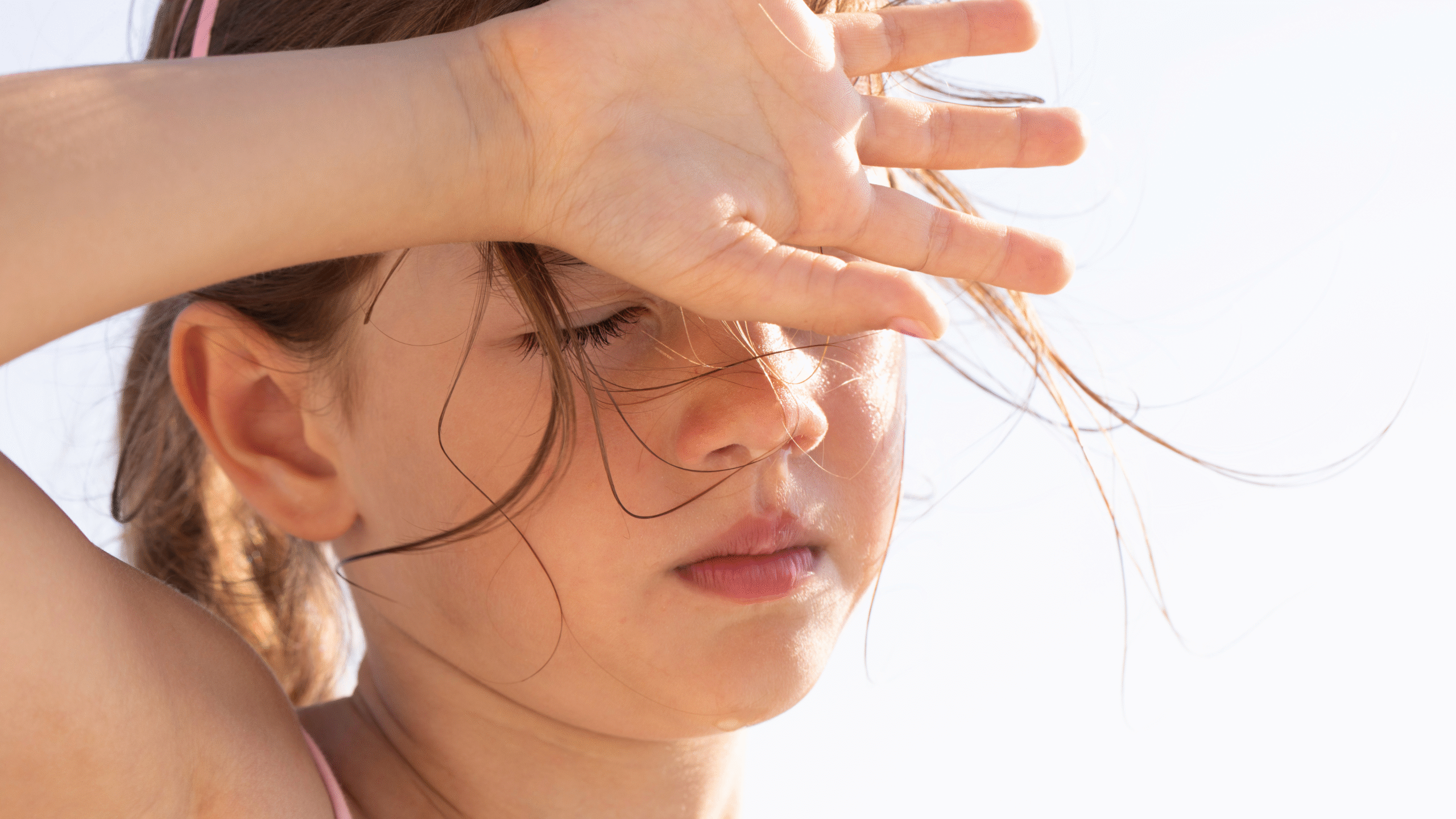 girl blocks the hot sun from her face with hand